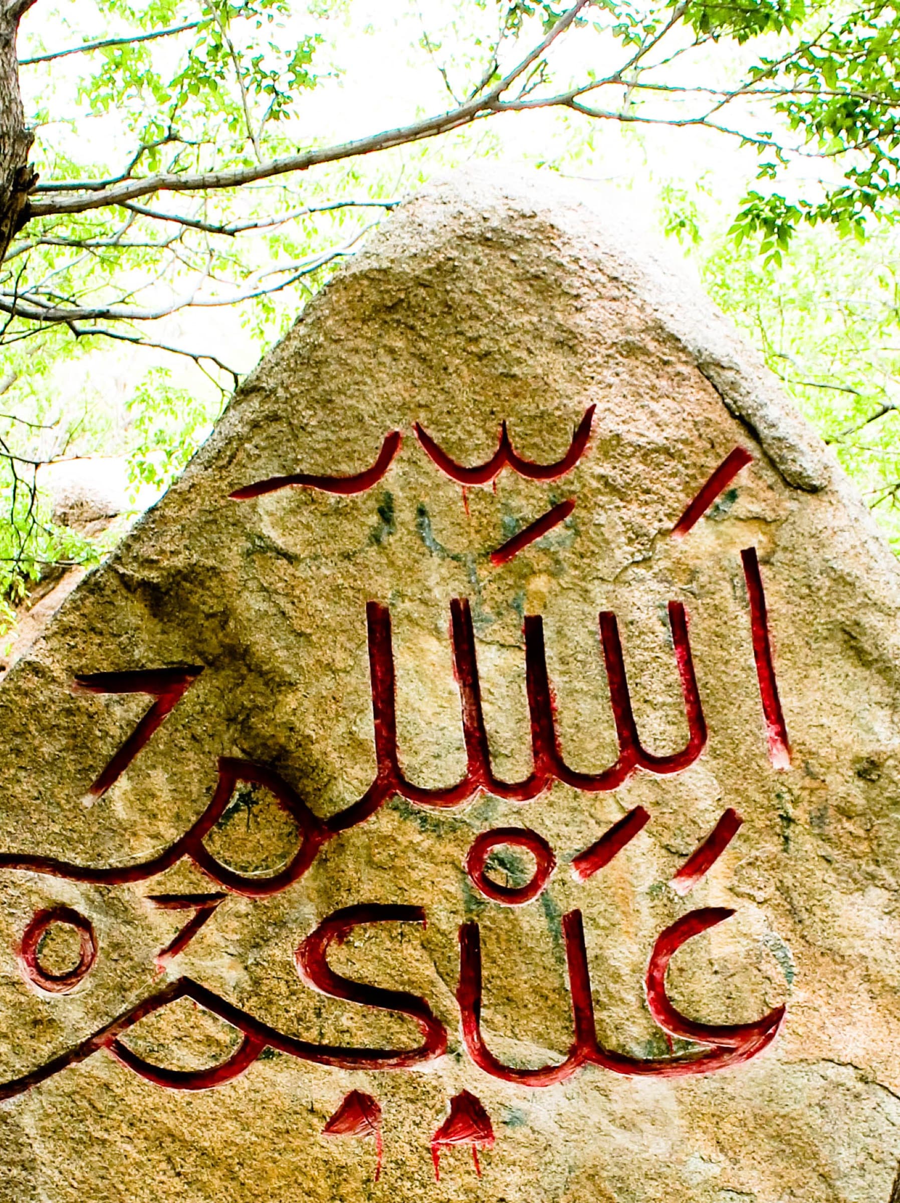 Bloc de rocher ocre à flanc de montagne, gravé et peint en jaune d’une inscription arabe.
